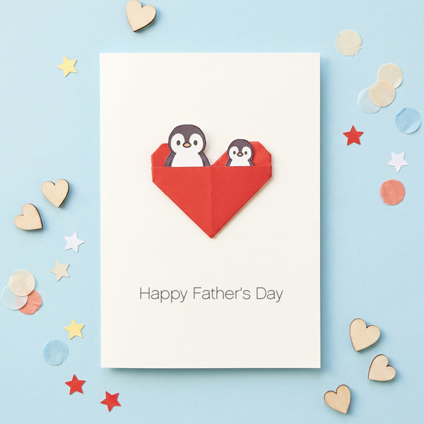 Cute handmade Father’s Day card featuring folded origami heart pocket on white card background. Daddy and baby penguin are tucked into the pocket of the heart. Underneath is says Happy Father's Day