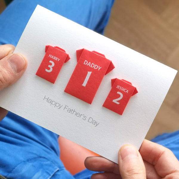 Father's Day football team card with red origami shirts labelled 'Harry', 'Daddy', and 'Jessica' on a white card. The football shirts depict Manchester United football club shirts and are origami shirts hand folded from paper. Underneath says Happy Father's Day
